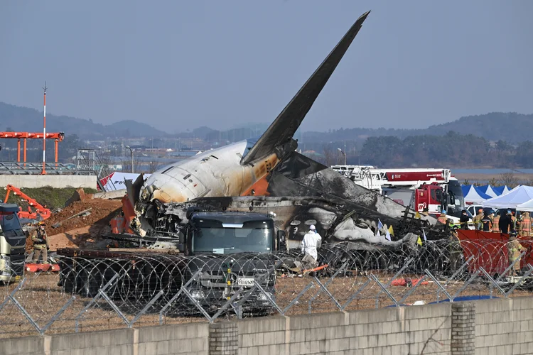 Bombeiros e equipes de resgate trabalham perto dos destroços do avião Boeing 737-800 da empresa sul-coreana Jeju Air que caiu no Aeroporto Internacional de Muan, cerca de 288 quilômetros a sudoeste de Seul, em 29 de dezembro de 2024 (JUNG YEON-JE / AFP/AFP Photo)