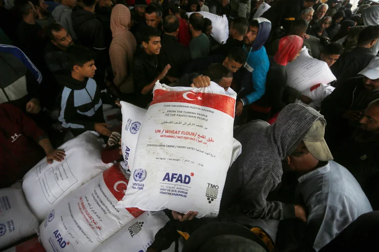 Palestinos fazem fila para receber farinha branca, distribuída pela Presidência Turca de Gestão de Desastres e Emergências (AFAD), no centro de distribuição da Agência das Nações Unidas de Assistência aos Refugiados da Palestina no Oriente Próximo (UNRWA) no Campo de Refugiados de Nuseirat em Deir al-Balah, Gaza, em 24 de novembro de 2024 (Ashraf Amra/Anadolu/Getty Images)