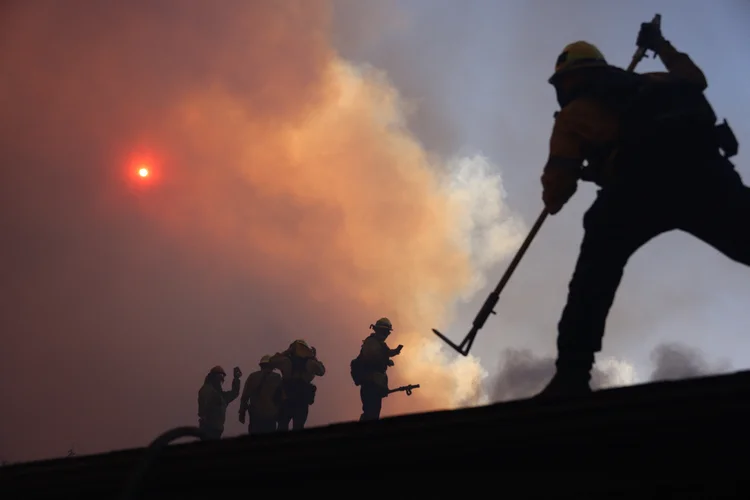 Bombeiros trabalham enquanto um incêndio florestal queima em Pacific Palisades, Califórnia, em 7 de janeiro de 2025. Um incêndio florestal de rápido avanço em um subúrbio de Los Angeles queimou prédios e provocou evacuações na terça-feira, enquanto ventos "com risco de morte" açoitavam a região. Mais de 200 acres (80 hectares) estavam queimando em Pacific Palisades, um local de luxo com casas multimilionárias nas Montanhas de Santa Monica, fechando uma rodovia importante e cobrindo a área com fumaça espessa (David Swanson/AFP)