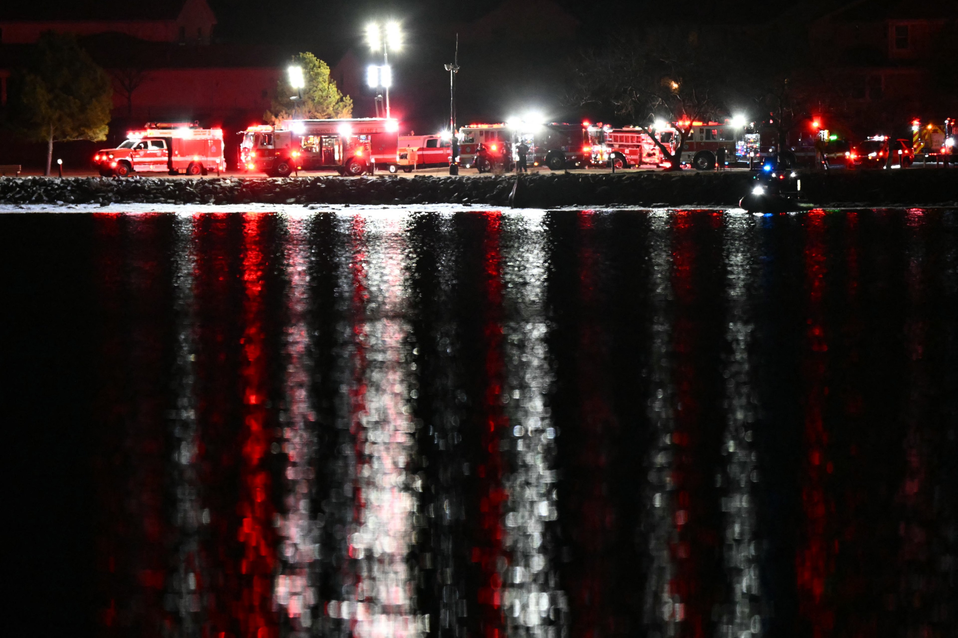 Veículos de emergência e equipes de resgate são vistos nas margens do Rio Potomac depois que um avião que se aproximava do Aeroporto Nacional Reagan caiu no rio fora de Washington, DC, em 30 de janeiro de 2025. Um jato regional do Kansas caiu no Rio Potomac, em Washington, após colidir no ar com um helicóptero militar perto do Aeroporto Nacional Reagan, disseram autoridades em 29 de janeiro, provocando uma grande resposta de emergência e paralisando todos os voos