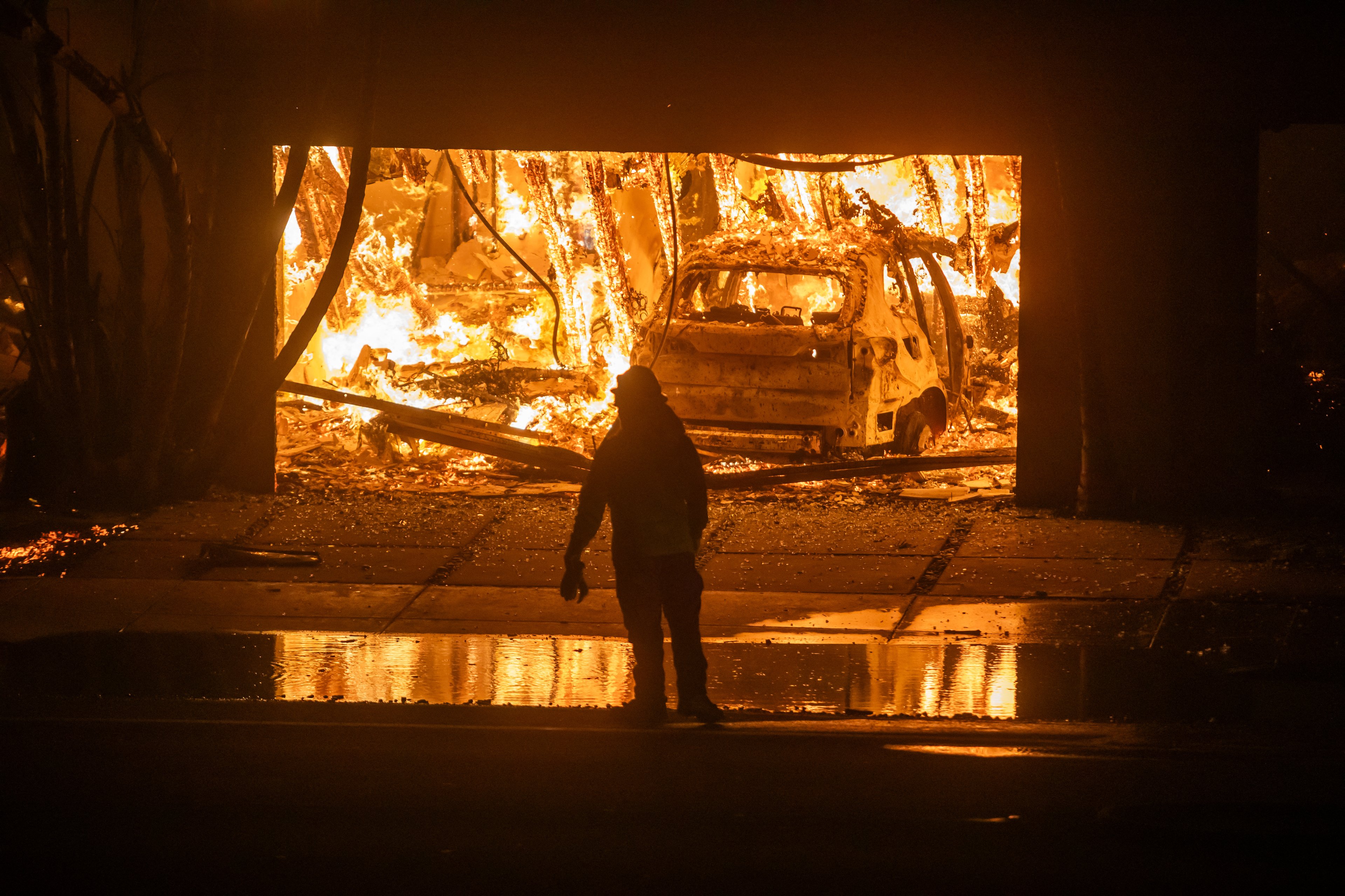 LOS ANGELES, CALIFORNIA - JANUARY 8: A firefighter watches the flames from the Palisades Fire burning homes on the Pacific Coast Highway amid a powerful windstorm on January 8, 2025 in Los Angeles, California. The fast-moving wildfire has grown to more than 2900-acres and is threatening homes in the coastal neighborhood amid intense Santa Ana Winds and dry conditions in Southern California.   Apu Gomes/Getty Images/AFP (Photo by Apu Gomes / GETTY IMAGES NORTH AMERICA / Getty Images via AFP)