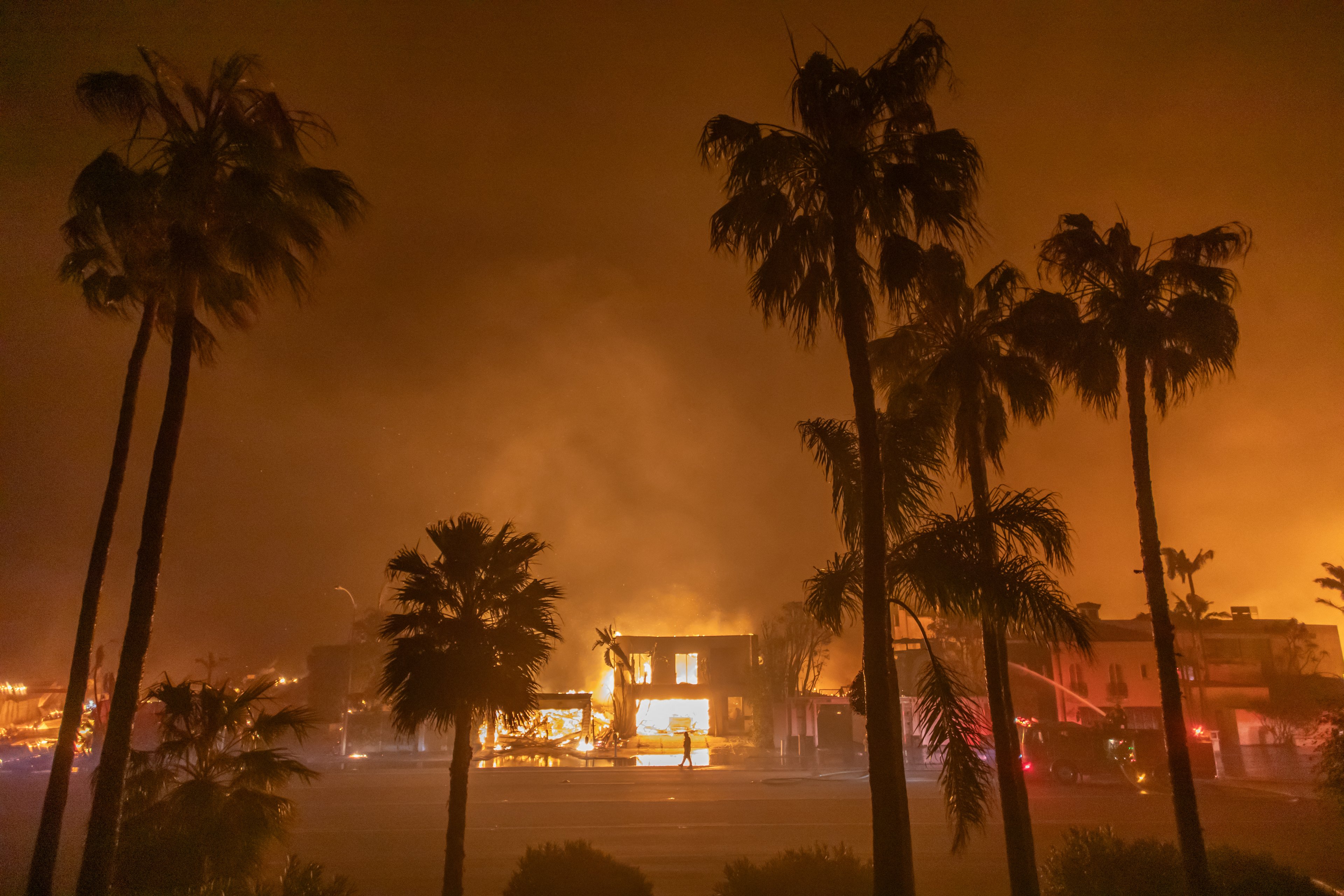 LOS ANGELES, CALIFORNIA - JANUARY 8: A firefighter watches the flames from the Palisades Fire burning homes on the Pacific Coast Highway amid a powerful windstorm on January 8, 2025 in Los Angeles, California. The fast-moving wildfire has grown to more than 2900-acres and is threatening homes in the coastal neighborhood amid intense Santa Ana Winds and dry conditions in Southern California.   Apu Gomes/Getty Images/AFP (Photo by Apu Gomes / GETTY IMAGES NORTH AMERICA / Getty Images via AFP)