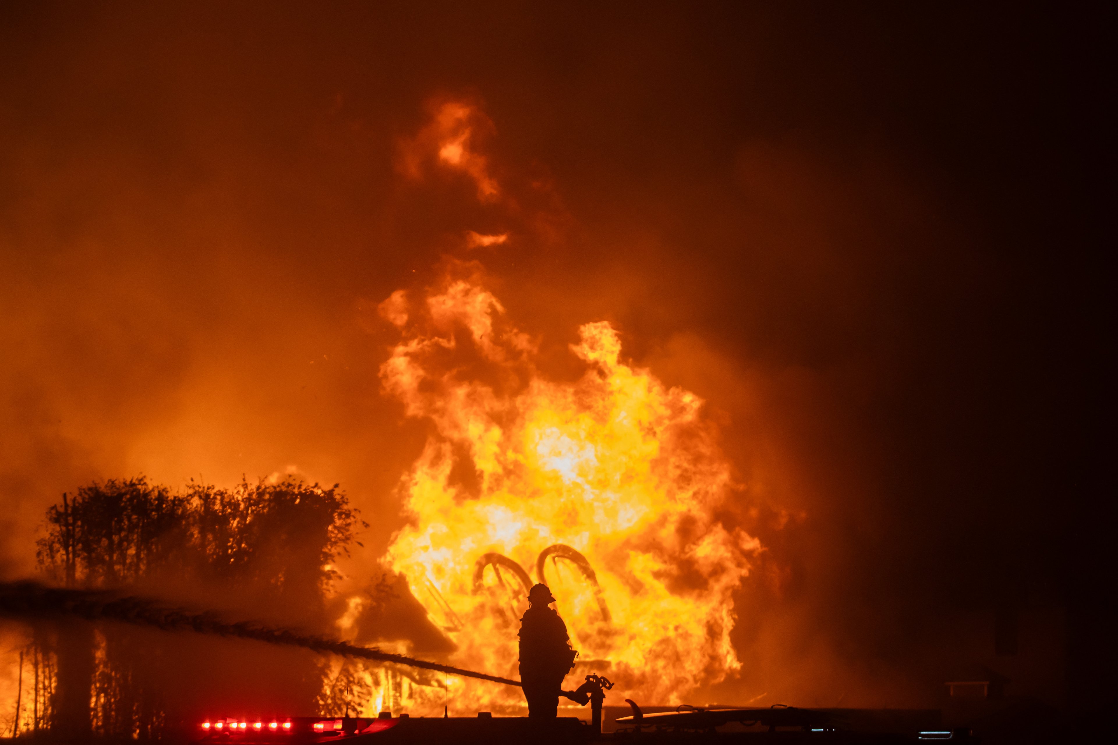 LOS ANGELES, CALIFORNIA - JANUARY 8: A firefighter stands on top of a fire truck to battle the Palisades Fire while it burns homes on the Pacific Coast Highway amid a powerful windstorm on January 8, 2025 in Los Angeles, California. The fast-moving wildfire has grown to more than 2900-acres and is threatening homes in the coastal neighborhood amid intense Santa Ana Winds and dry conditions in Southern California.   Apu Gomes/Getty Images/AFP (Photo by Apu Gomes / GETTY IMAGES NORTH AMERICA / Getty Images via AFP)