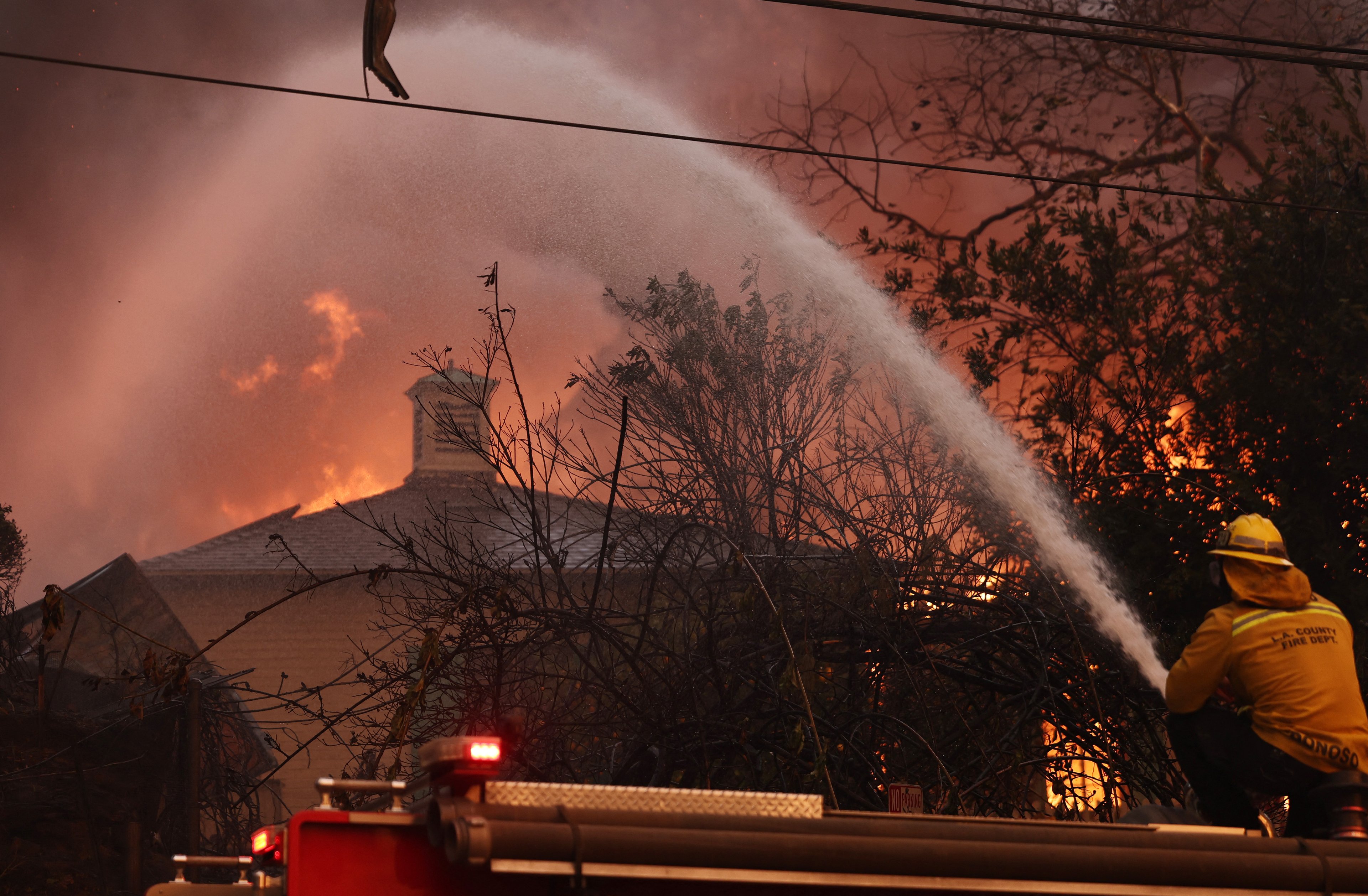 ALTADENA, CALIFORNIA - JANUARY 08: A firefighter sprays water as a home burns during the Eaton Fire on January 8, 2025 in Altadena, California. Over 1,000 structures have burned, with two people dead, in wildfires fueled by intense Santa Ana Winds across L.A. County.   Mario Tama/Getty Images/AFP (Photo by MARIO TAMA / GETTY IMAGES NORTH AMERICA / Getty Images via AFP)