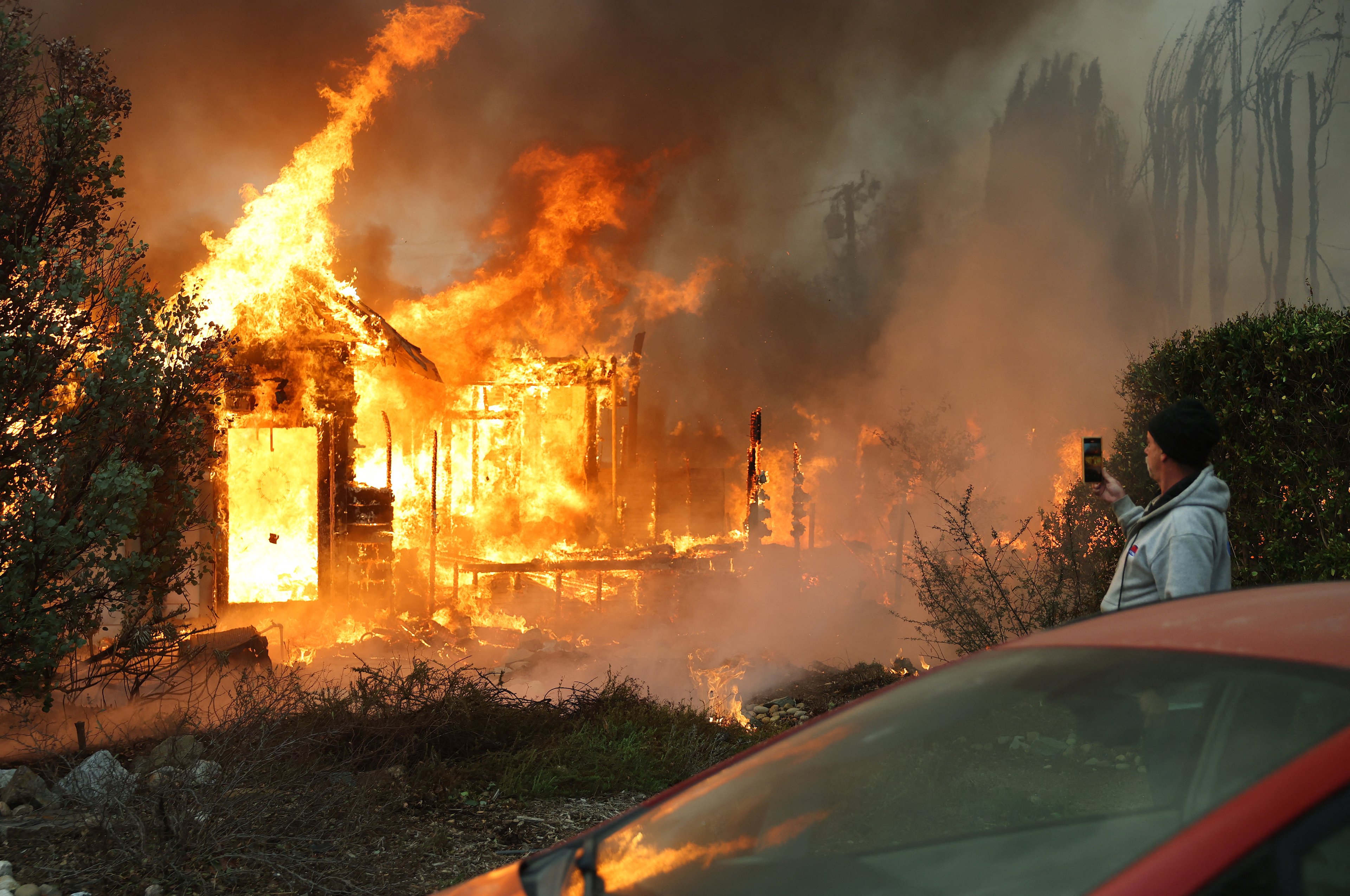 ALTADENA, CALIFORNIA - JANUARY 08: A person views a home burning during the Eaton Fire on January 8, 2025 in Altadena, California. Over 1,000 structures have burned, with two people dead, in wildfires fueled by intense Santa Ana Winds across L.A. County.   Mario Tama/Getty Images/AFP (Photo by MARIO TAMA / GETTY IMAGES NORTH AMERICA / Getty Images via AFP)