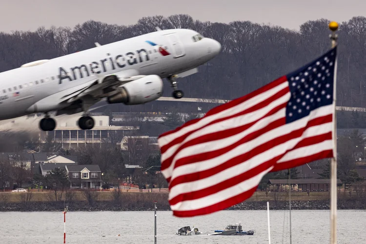 Avião decola do aeroporto Reagan enquanto, ao fundo, equipes de busca seguem trabalhando no rio Potomac (Al Drago /AFP)