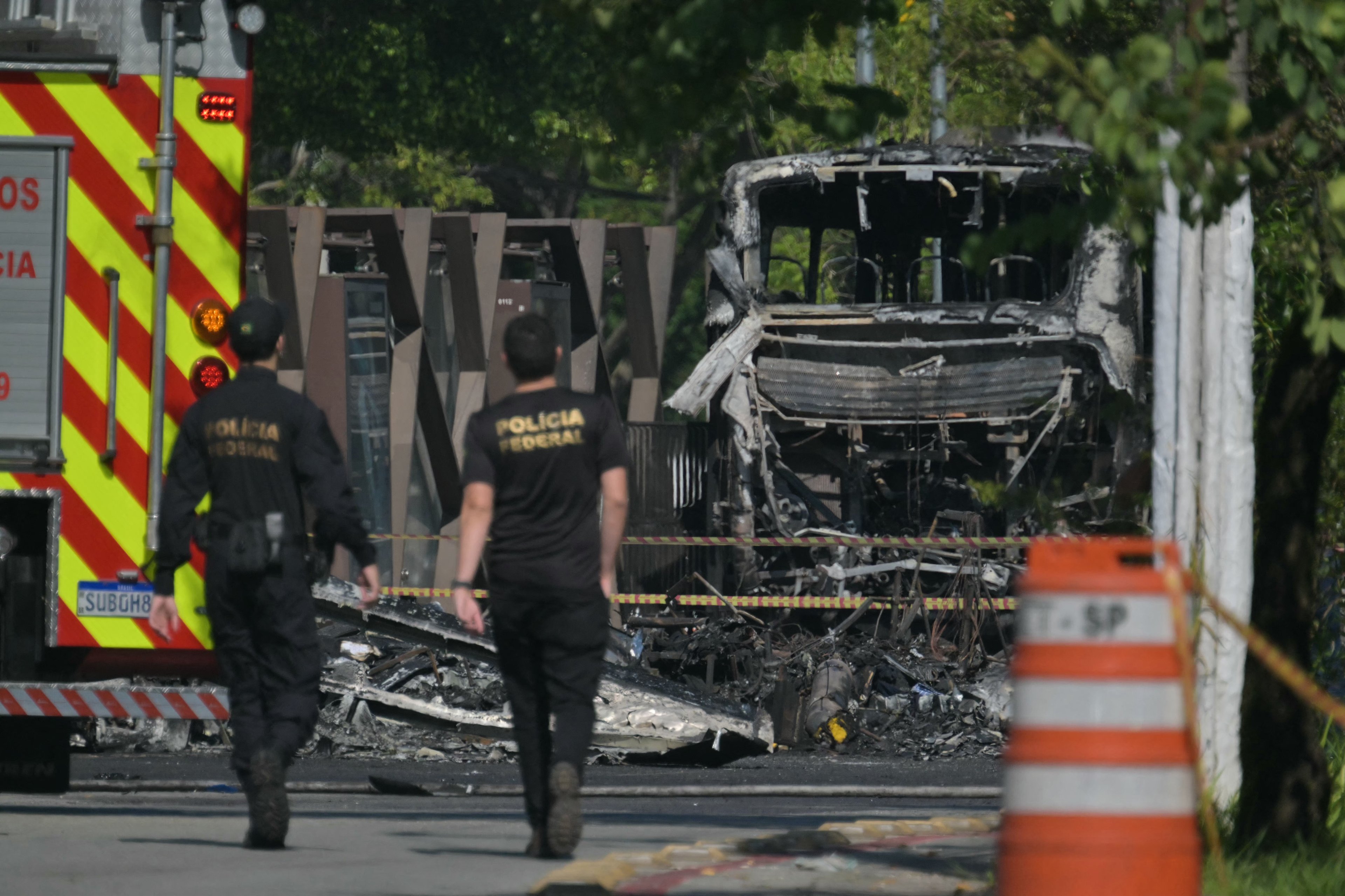 Membros da Polícia Federal caminham em frente aos destroços de um ônibus atingido por um avião que caiu em uma avenida em São Paulo, Brasil, em 7 de fevereiro de 2025. Um avião caiu em uma grande avenida na cidade brasileira de São Paulo na sexta-feira e explodiu após atingir um ônibus, deixando duas pessoas mortas e seis feridas, disseram autoridades. (Foto de NELSON ALMEIDA / AFP)