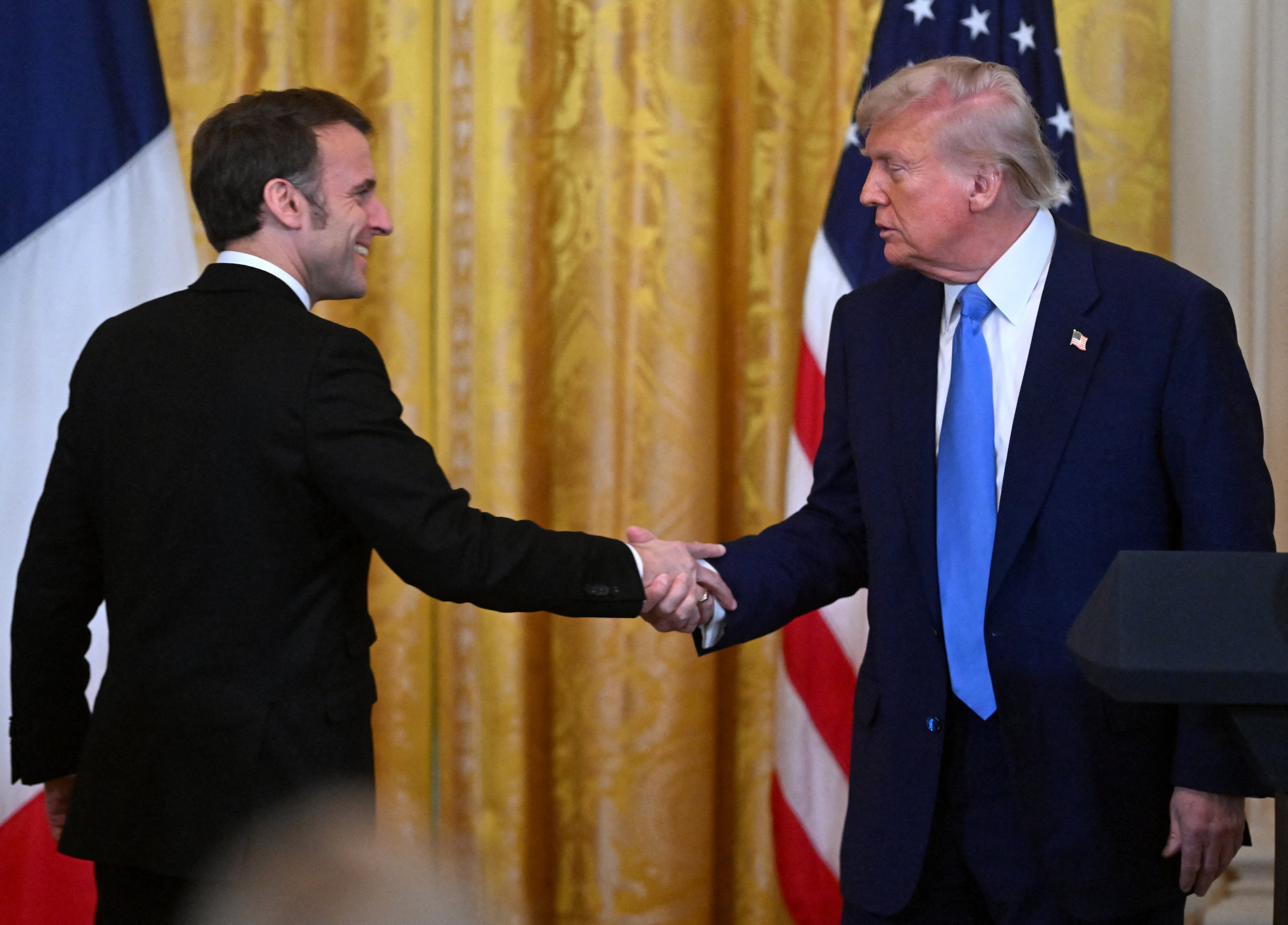 O presidente dos EUA, Donald Trump, e o presidente francês, Emmanuel Macron, apertam as mãos no final de uma entrevista coletiva conjunta no Salão Leste da Casa Branca, em Washington, DC, em 24 de fevereiro de 2025. (Foto de ROBERTO SCHMIDT / AFP)