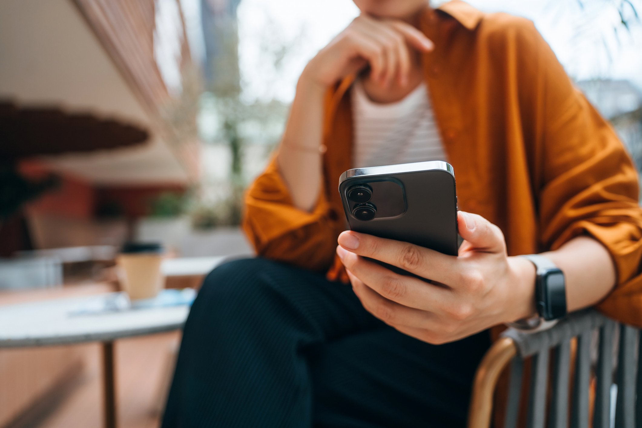 Close up shot of a young Asian woman using smartphone while sitting in an outdoor cafe and drinking coffee. Lifestyle and technology