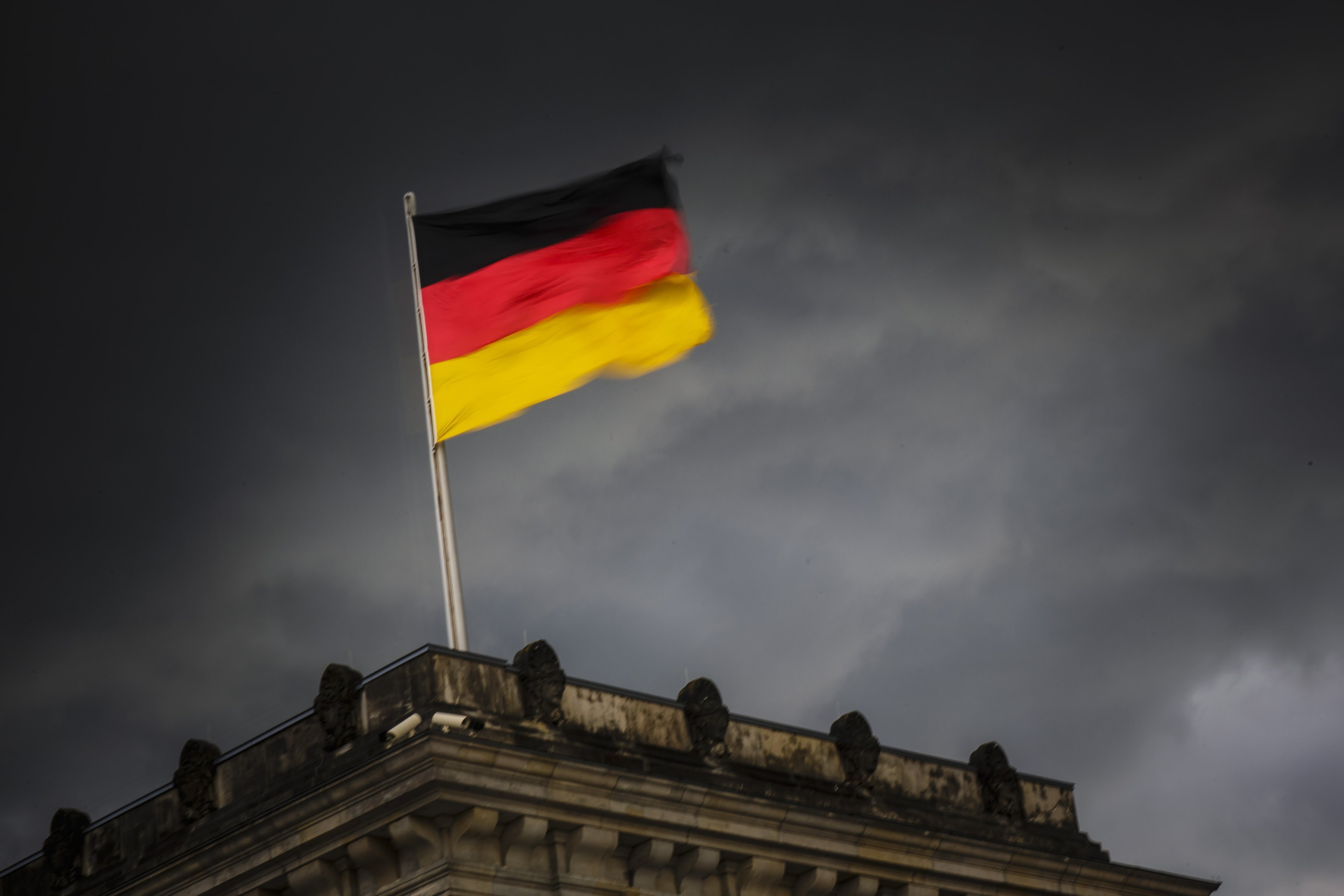 A bandeira nacional da Alemanha tremula no edifício do Reichstag diante de um céu com nuvens escuras em Berlim,