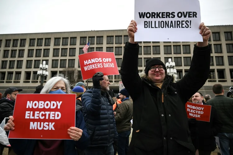 Manifestantes seguram cartazes durante um protesto contra o presidente dos EUA, Donald Trump, e o Doge, a comissão confiada a Elon Musk (AFP)