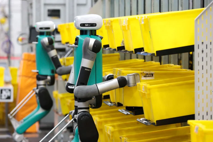 Robôs bípedes em fase de testes movem contêineres durante uma demonstração de manipulação móvel no evento "Delivering the Future" da Amazon no BFI1 Fulfillment Center da empresa, Robotics Research and Development Hub em Sumner, Washington (JASON REDMOND/Getty Images)