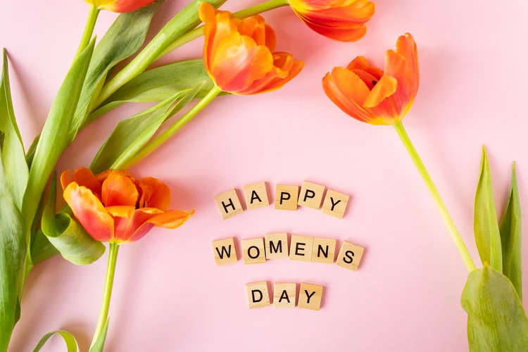 March 8, postcard. Happy Women's Day text sign with orange tulips on pink background. Stylish flat lay with flowers and text, greeting card (Envato Divulgação)