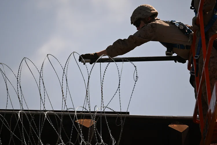 Militar instala arame farpado em cima de muro na fronteira entre EUA e México, perto de San Diego (Patrick T. Fallon/AFP)