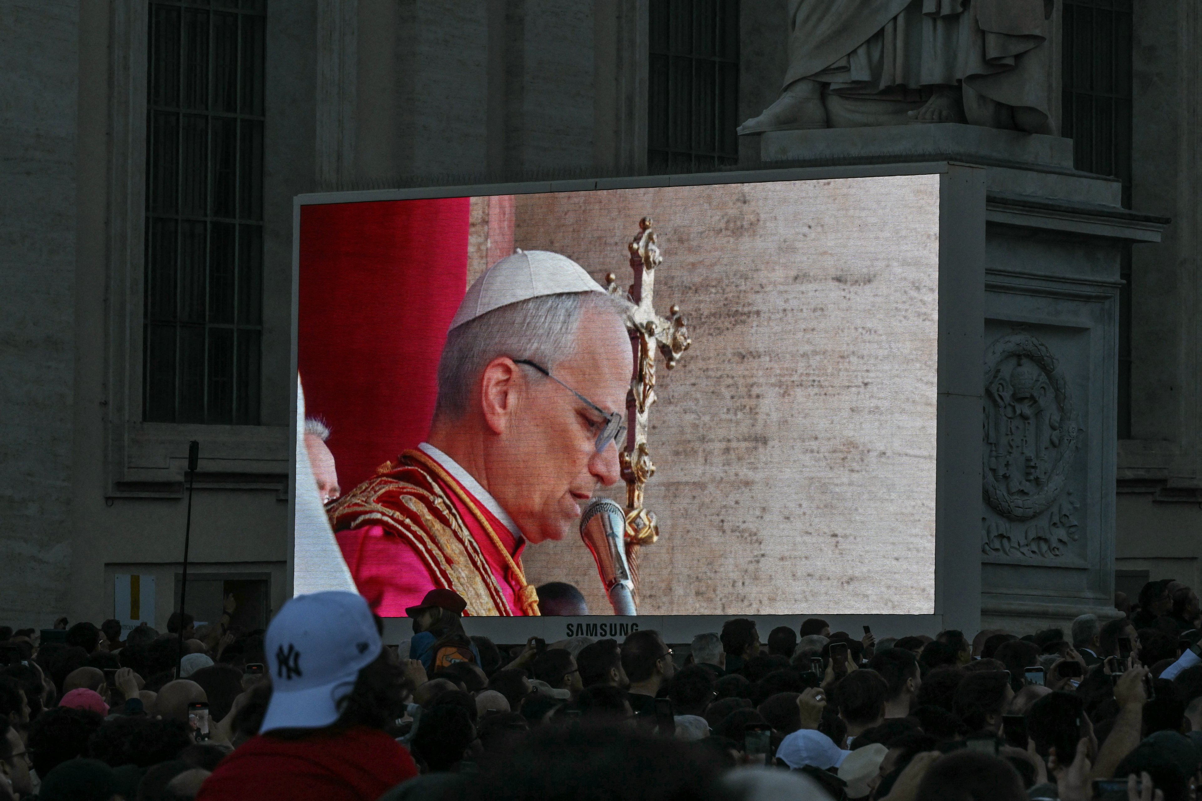 Pessoas assistem a um telão enquanto o recém-eleito Papa Robert Francis Prevost, Papa Leão XIV, se dirige à multidão pela primeira vez na varanda principal da galeria central da Basílica de São Pedro