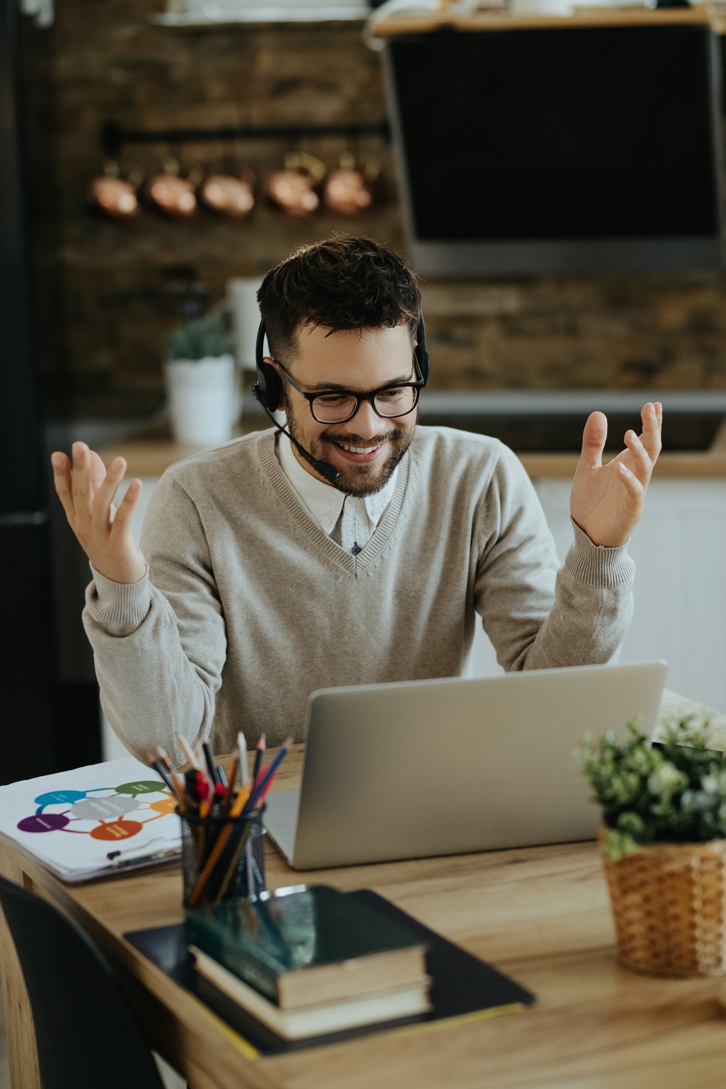 Happy businessman with headphones talking to someone while making video call over laptop from home.