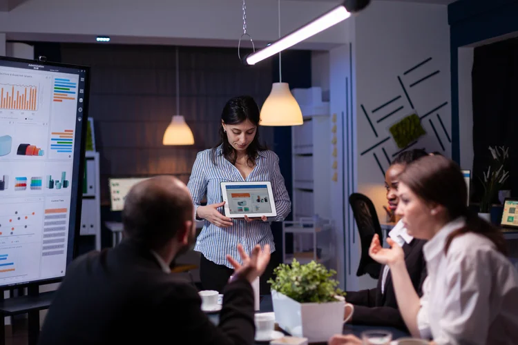 Overworked workaholic entrepreneur woman shwoing marketing graphs using tablet overworking at company solution late at night in meeting room. Diverse multi-ethnic teamwork solving financial strategy (Freepik)