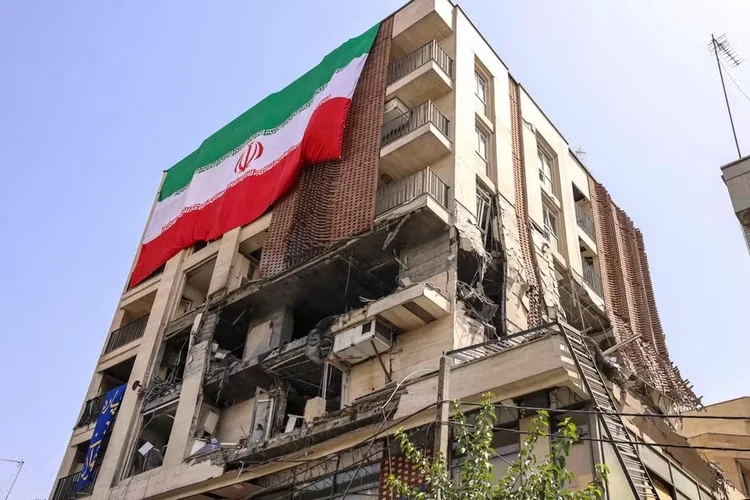 Bandeira do Irã cobre parcialmente prédio atingido por míssil israelense em Teerã  ( ATTA KENARE / AFP)