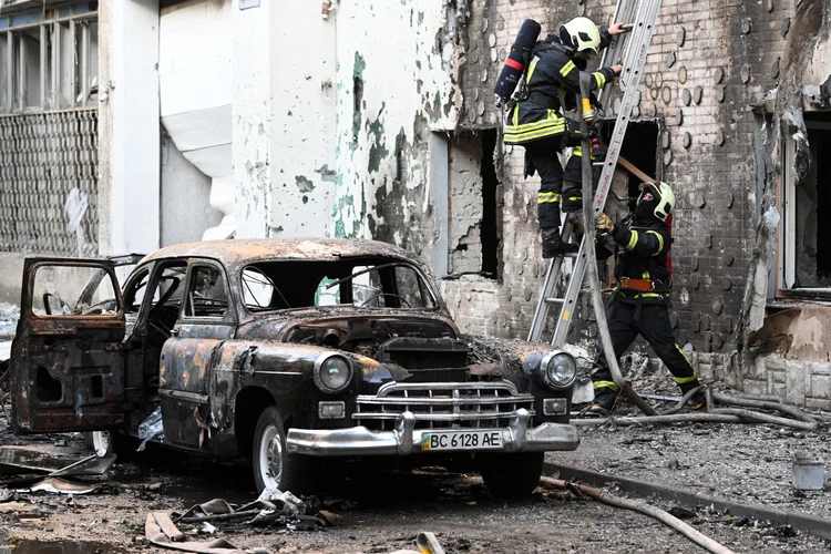 Bombeiros são vistos ao lado de um carro queimado após ataques em massa de drones e mísseis russos na cidade de Lviv, no oeste da Ucrânia, em 12 de julho de 2025, em meio à invasão russa da Ucrânia. (YURIY DYACHYSHYN / AFP/AFP Photo)