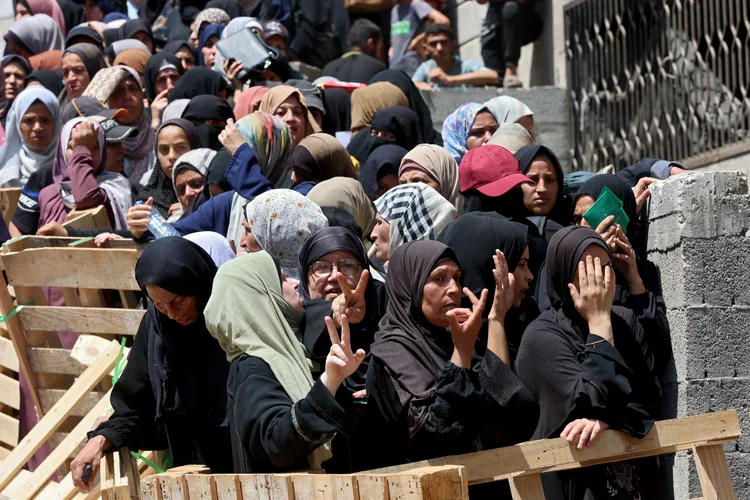 Mulheres palestinas fazem o sinal de V de vitória enquanto fazem fila para receber sacos de farinha em um depósito do Programa Mundial de Alimentos (PMA) da ONU na rua Al-Jalaa, na Cidade de Gaza, no centro da Faixa de Gaza, em 12 de julho de 2025. (Omar AL-QATTAA / AFP/AFP)