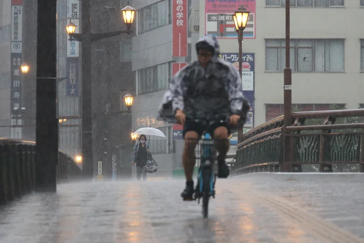 Chuvas no Japão: pessoas caminham e pedalam sob forte chuva na cidade de Kumamoto, no sudoeste do país, em 11 de agosto de 2025. (STR/JIJI Press/AFP/Getty Images)