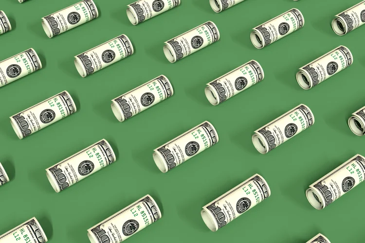 Notas de dólar enroladas sobre uma superfície verde. Padrão criativo de dinheiro. As notas estão dispostas na diagonal. Ilustração 3D.
 (Julia Kuznetsova/Getty Images)