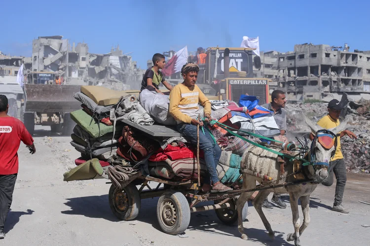 Displaced people transport their belongings on a donkey cart, past bulldozers deployed by the Gaza Municipality on their way to clear building rubble from main axes and streets in Gaza City, amid a ceasefire between Israel and Palestinian factions, on October 14, 2025. (Photo by AFP) (AFP/AFP)