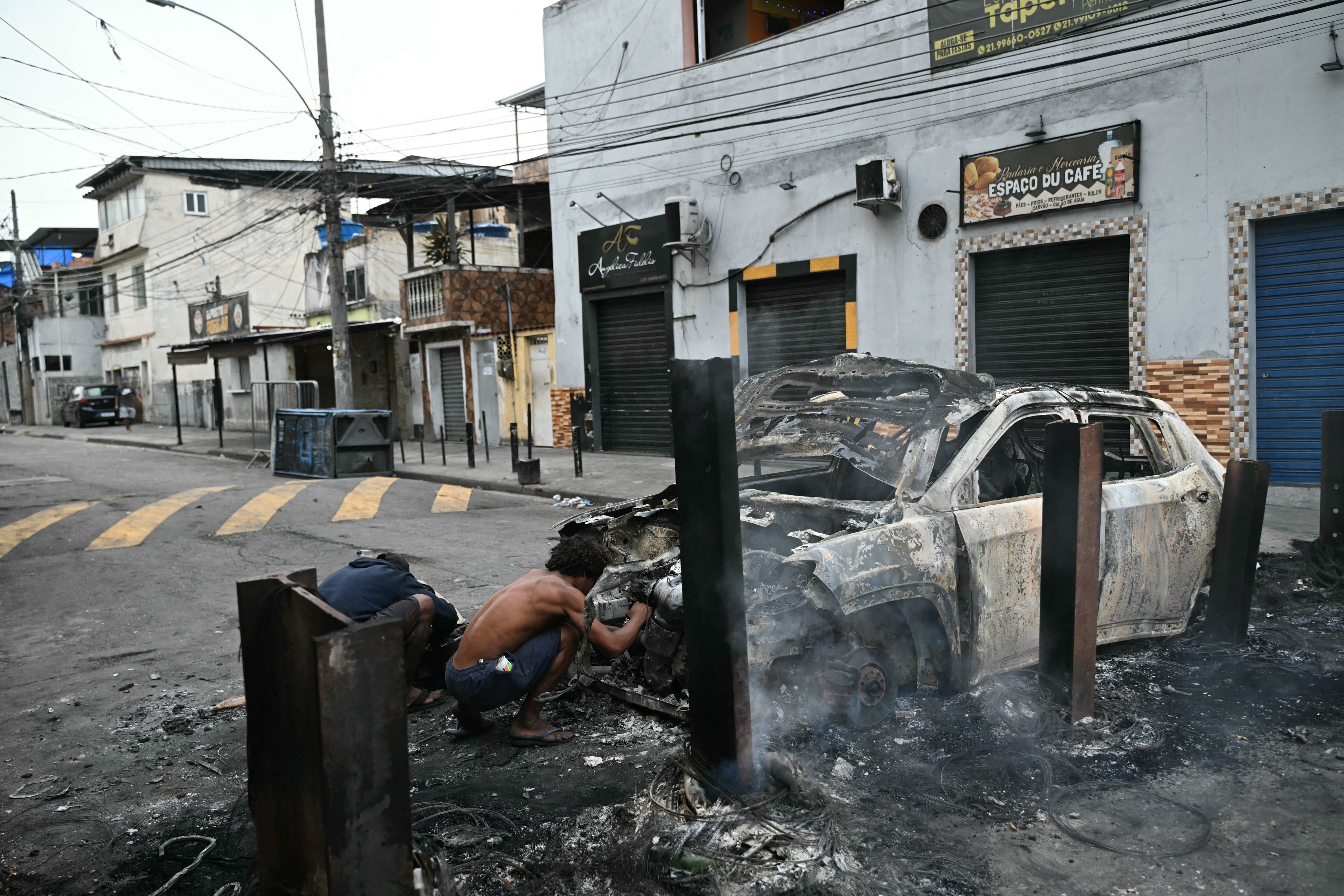 Homens inspecionam um carro incendiado que fazia parte de uma barricada montada durante a Operação Contenção na favela da Vila Cruzeiro, no complexo da Penha, no Rio de Janeiro nesta terça-feira, 28