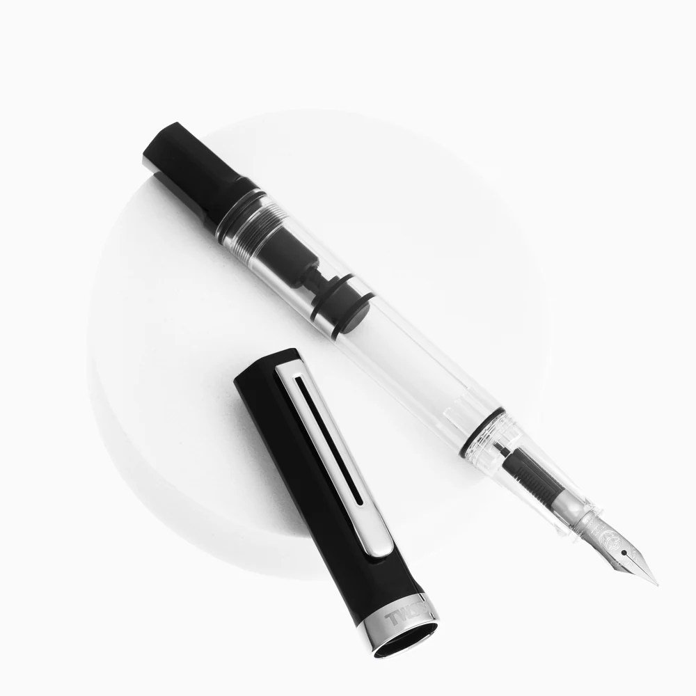 Caneta tinteiro TWSBI ECO preta com corpo transparente e tampa preta com detalhe metálico, exibida em diagonal sobre fundo branco com a tampa removida ao lado.