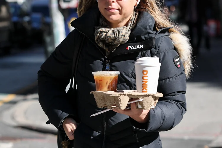 Uma mulher caminha carregando uma bandeja com bebidas de café na cidade de Nova York, em 16 de outubro de 2025 (Angela Weiss/AFP)
