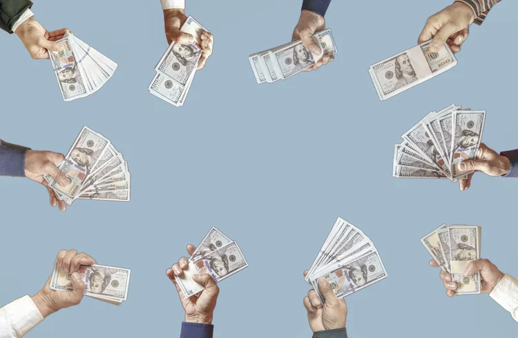 Várias mãos segurando notas de dólares em um fundo azul (Getty Images)