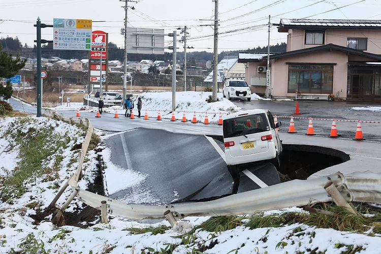 Um veículo permanece à beira de uma estrada que desabou na cidade de Tohoku, na província de Aomori, em 9 de dezembro de 2025, após um terremoto de magnitude 7,5 no norte do Japão. Um forte tremor na região norte do país deixou ao menos 30 feridos, segundo autoridades, danificou estradas e provocou falta de energia para milhares de pessoas em meio a temperaturas congelantes. (Getty Images)