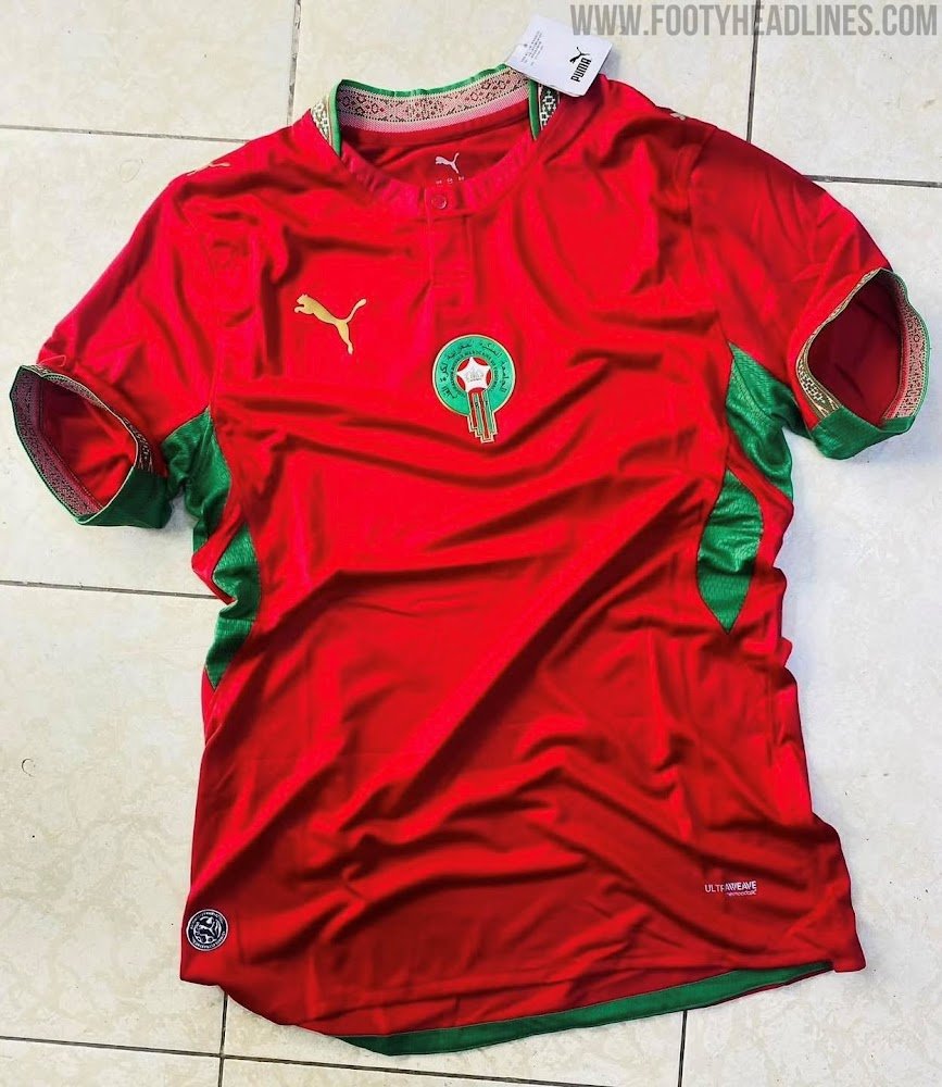 vermelho predominante com motivos culturais nas golas e punhos e painéis laterais verdes; desenhos inspirados na arte marroquina aparecem de forma sutil