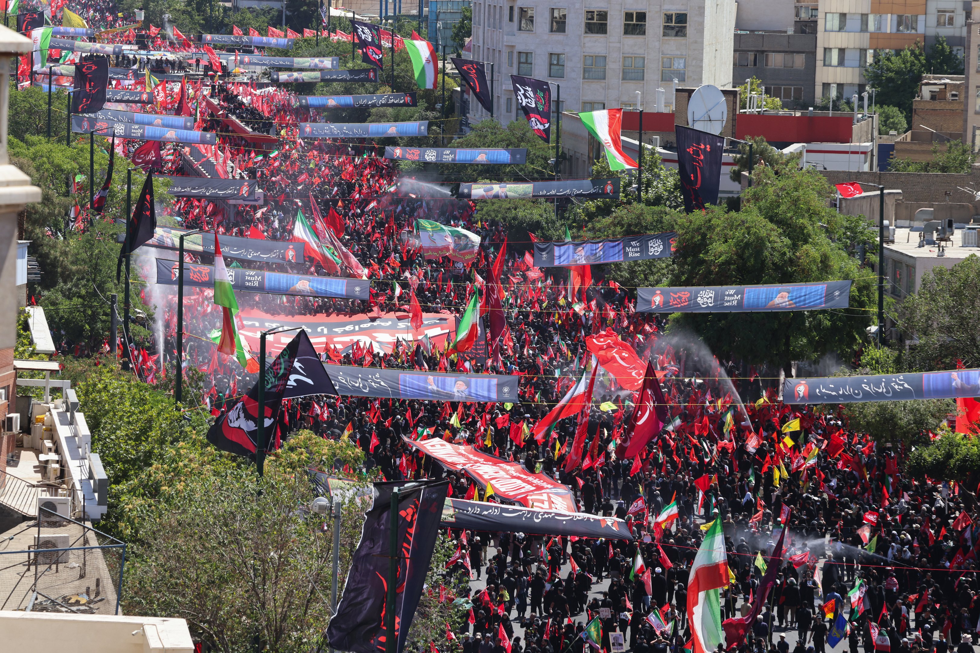 Pessoas em luto marcham com bandeiras e faixas durante o cortejo fúnebre do falecido líder supremo do Irã, Ali Khamenei, e de membros de sua família, antes de seu sepultamento no Santuário do Imam Reza — o local de culto mais venerado do Irã —, em Mashhad, em 9 de julho de 2026. Enfrentando um calor intenso e clamando por vingança, iranianos leais à República Islâmica reuniram-se em massa, em 9 de julho, para o sepultamento do falecido líder supremo Ali Khamenei em sua cidade natal, Mashhad