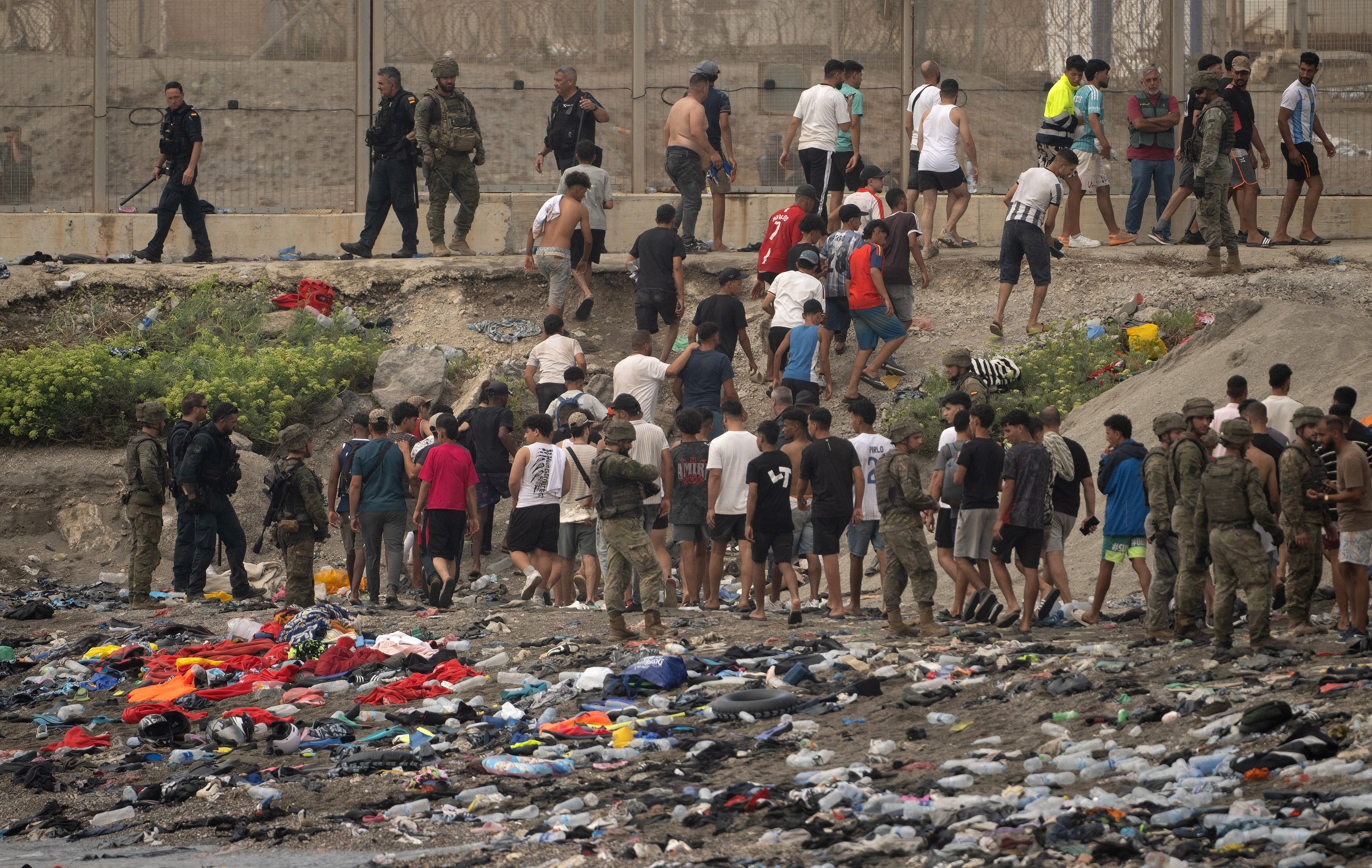 Soldados espanhóis orientam grupo de migrantes na praia durante retorno para o Marrocos na fronteira de Ceuta.