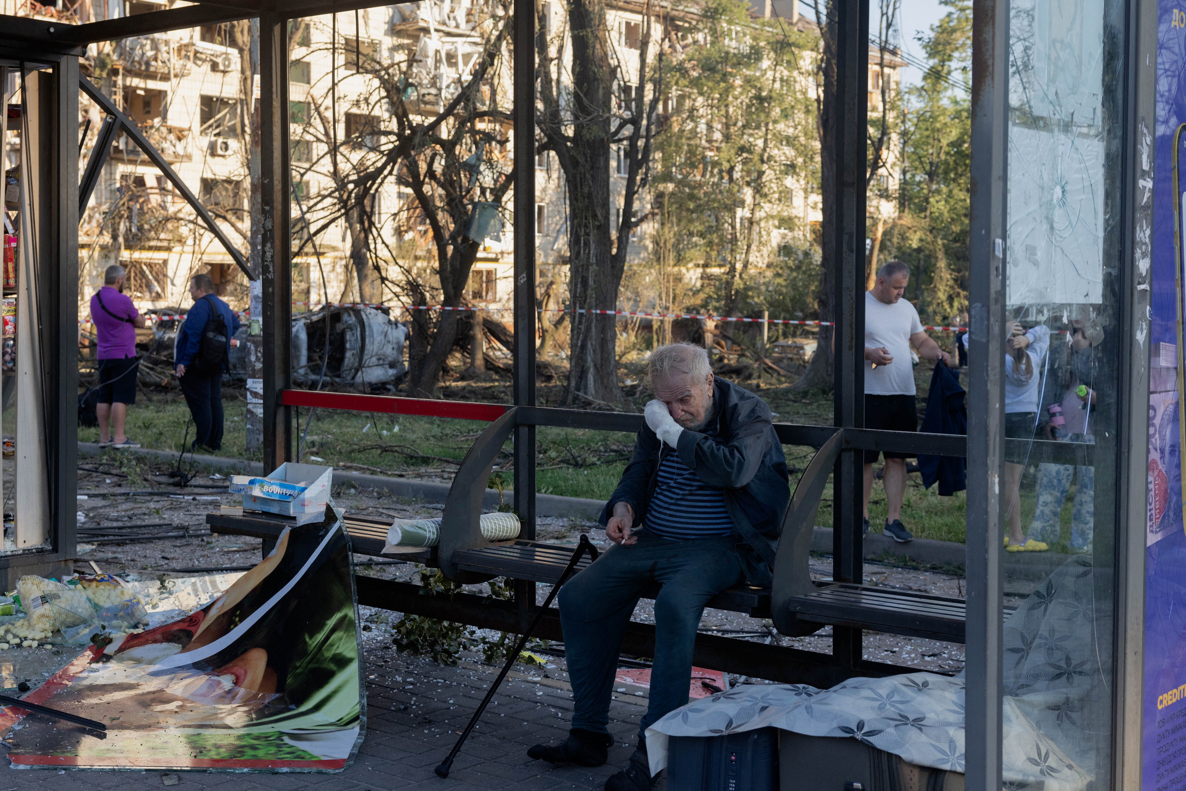 Um homem com o braço enfaixado está sentado em uma parada de ônibus danificada, perto de um prédio residencial também avariado após um ataque aéreo russo à capital ucraniana, Kiev, em 2 de julho de 2026, em meio à invasão russa da Ucrânia. Ataques russos com mísseis e drones atingiram Kiev nas primeiras horas de 2 de julho, matando pelo menos oito pessoas e deixando dezenas de feridos, depois que o presidente Volodymyr Zelensky alertou que Moscou estava preparando um 