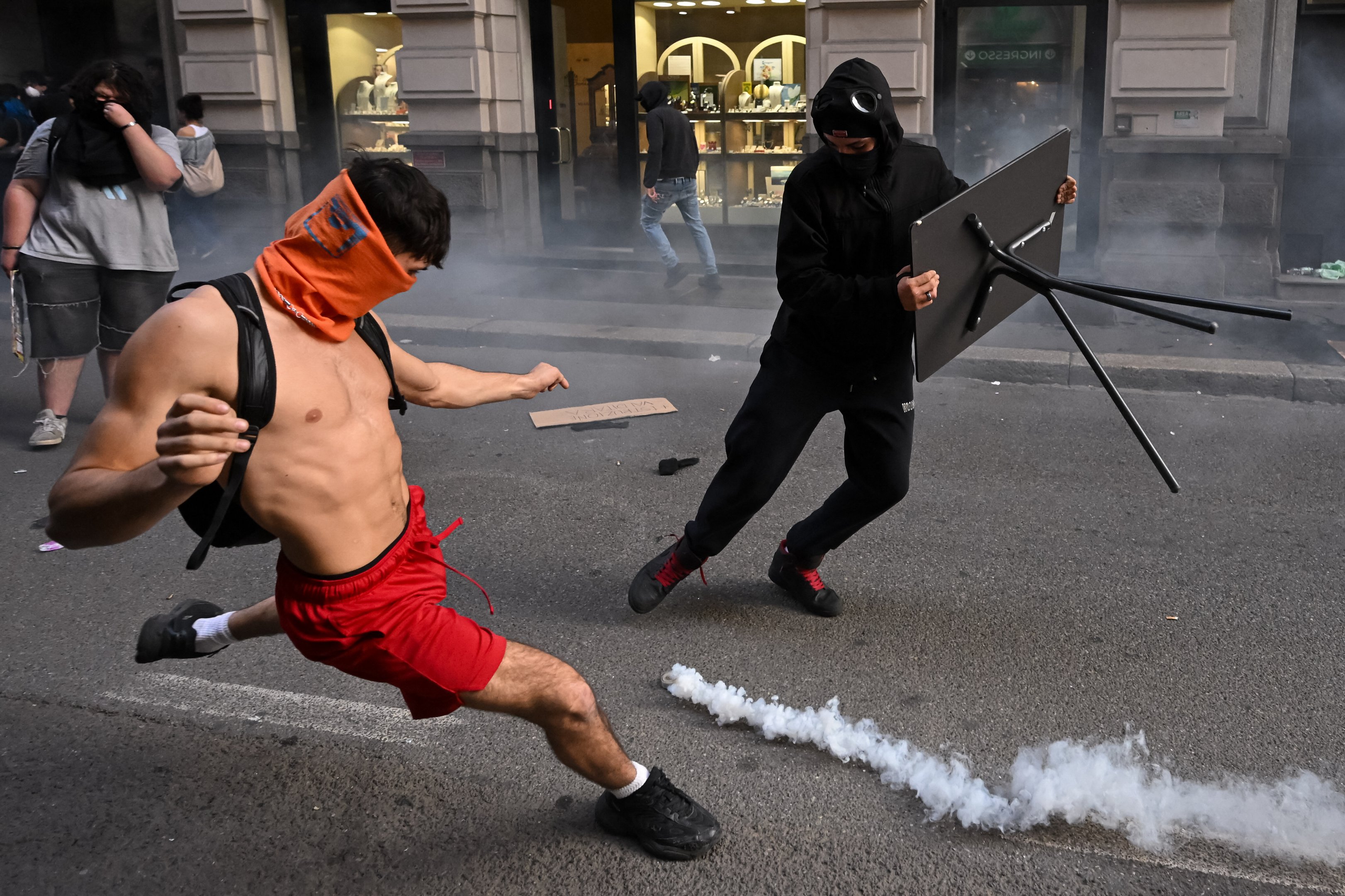 Manifestante chuta lata de gás lacrimogêneo durante confronto com a polícia em Milão, na Itália