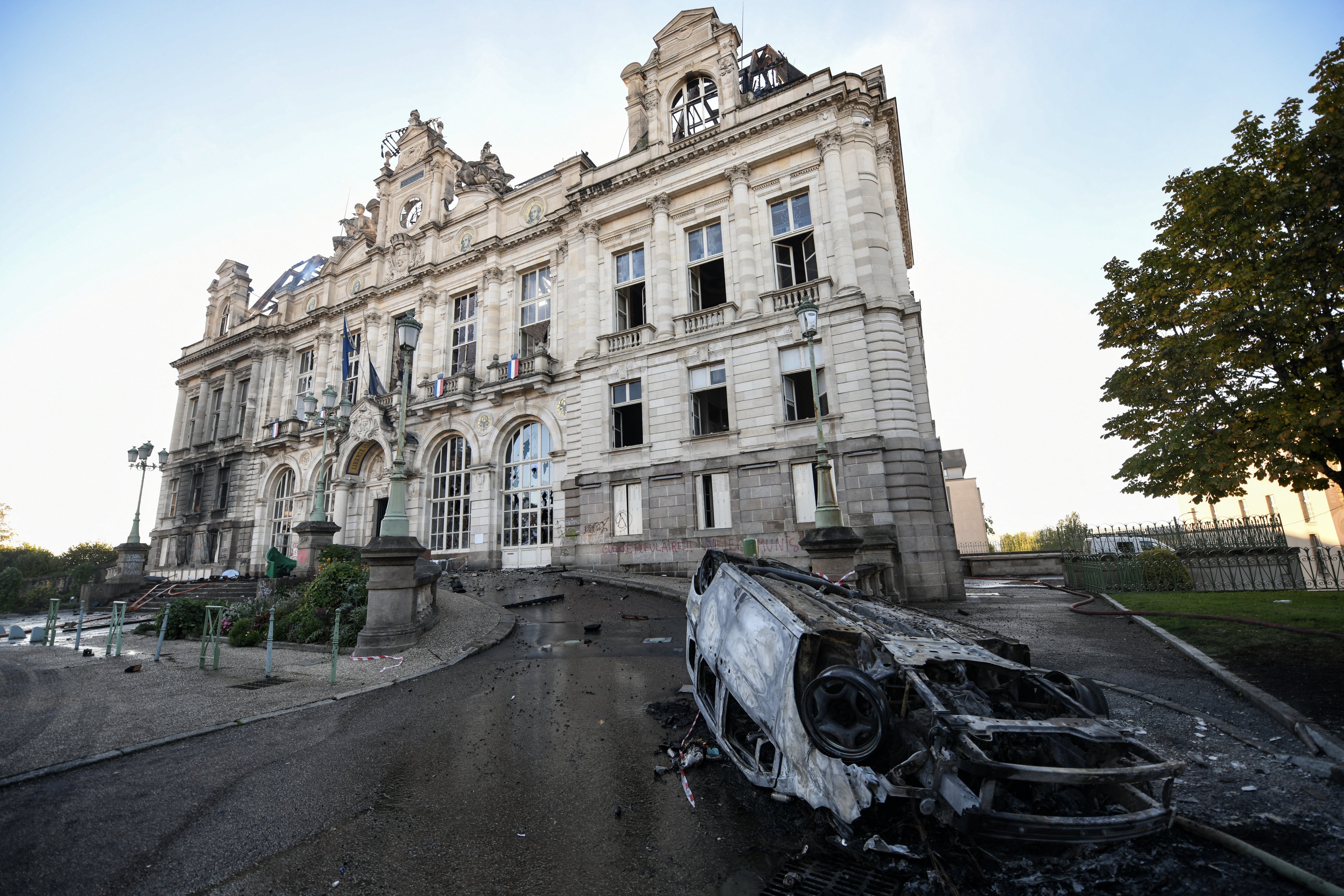 Esta fotografia mostra os destroços de um veículo incendiado e a fachada parcialmente queimada da prefeitura de Limoges, um dia após os tumultos e saques que se seguiram aos protestos em todo o país contra o 
